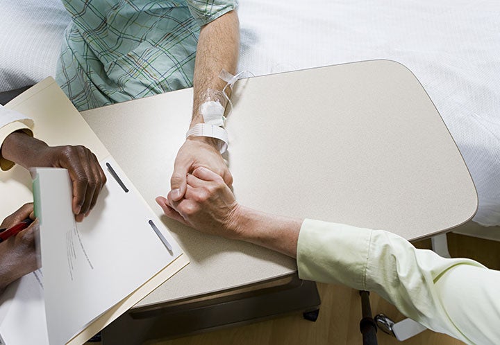 A patient and family member holding hands and a doctor writing on a clipboard.
