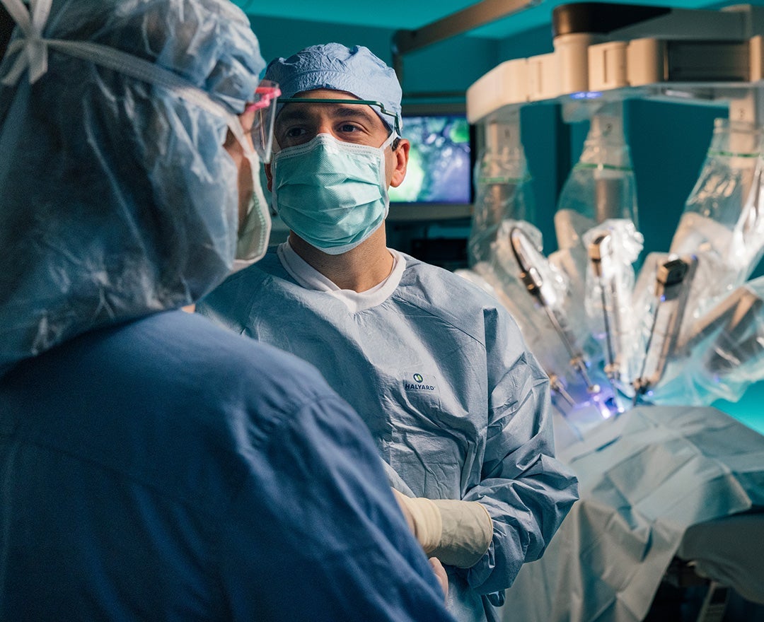 Dr. Giannone, a general surgeon in full medical PPE, talks to a surgical assistant - a da Vinci surgical robot is behind him.